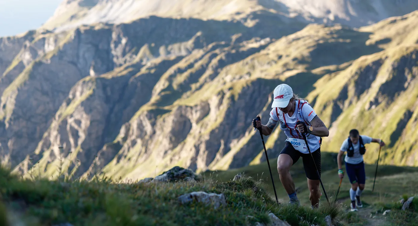 Corredora del equipo Altra subiendo una montaña con bastones